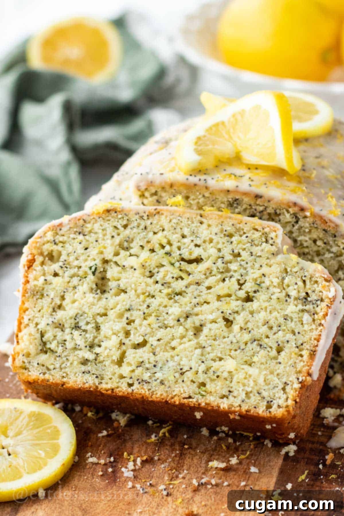 Slice of lemon zucchini bread next to baked loaf on wood cutting board with lemon slice.