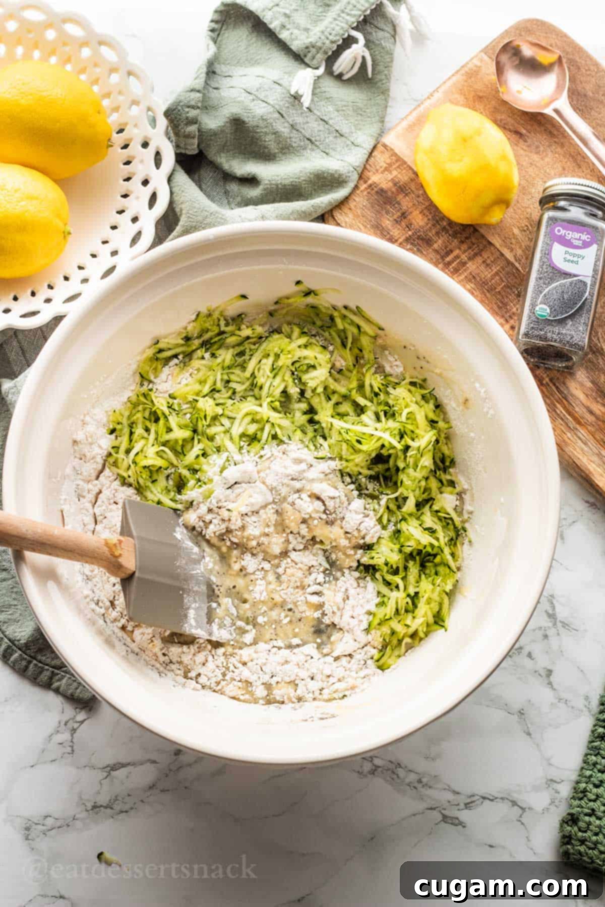White mixing bowl with wet and dry ingredients for lemony zucchini bread.