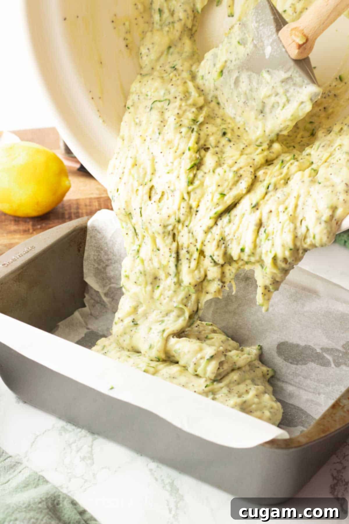 White bowl pouring wet batter into metal bread pan lined with parchment paper.