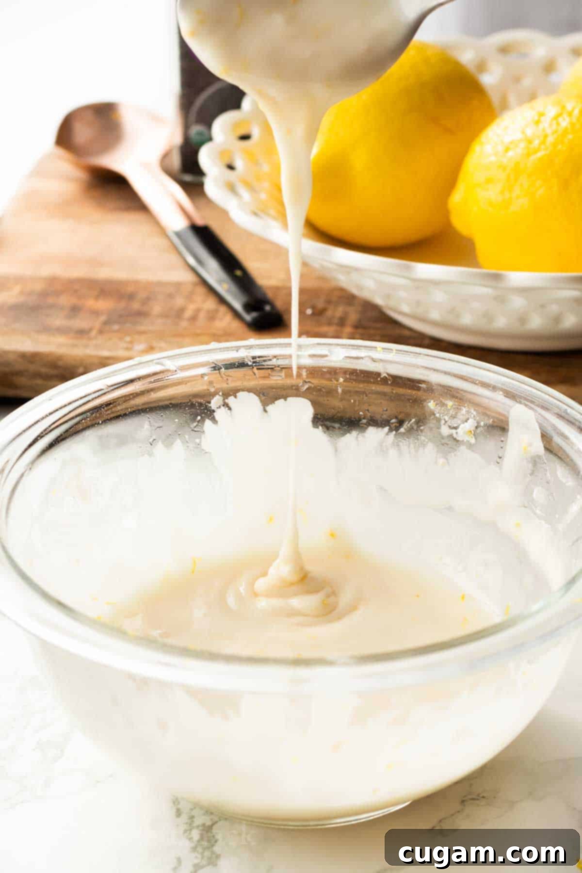 Spoon drizzling lemon icing into glass bowl.