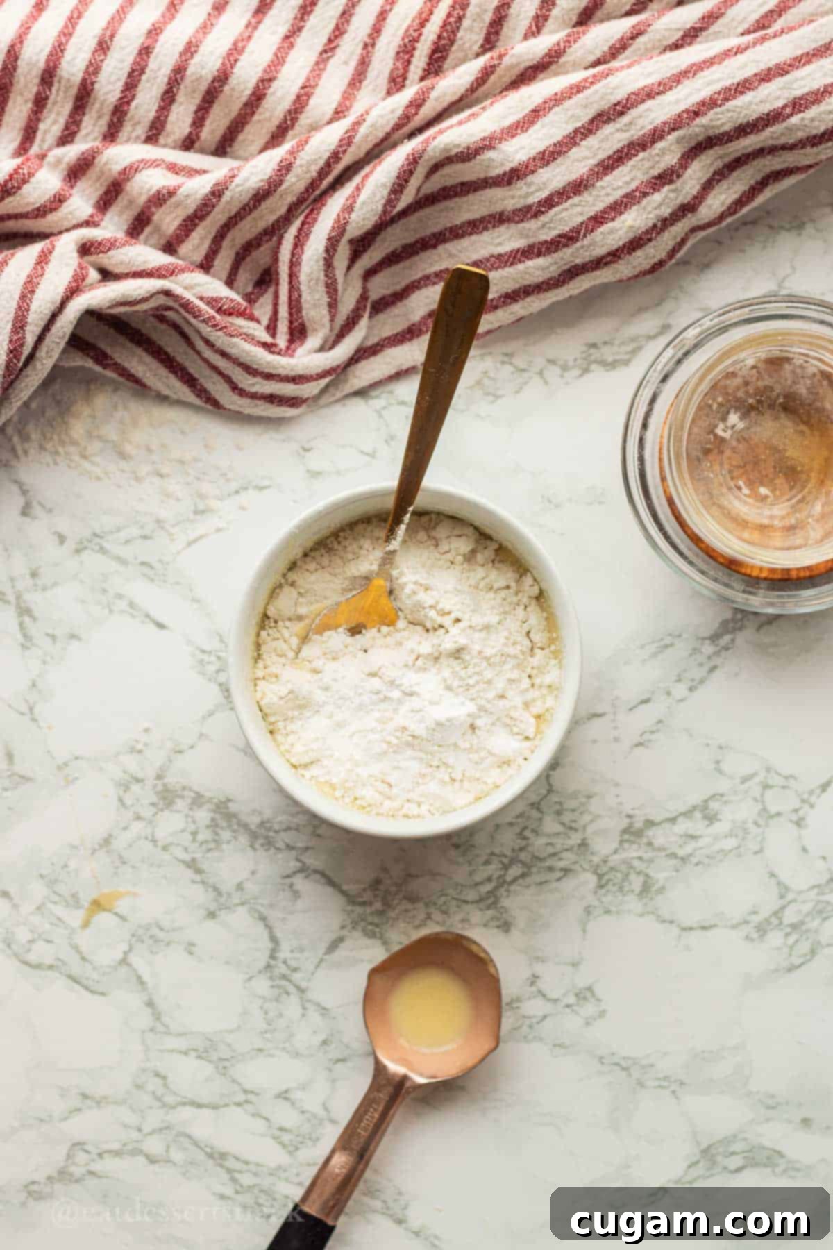Flour and baking powder in white bowl with gold spoon, about to be added to wet ingredients.