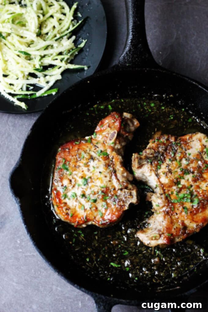 Brown sugar pork chops with garlic and herbs in a skillet, zucchini noodles on a plate.