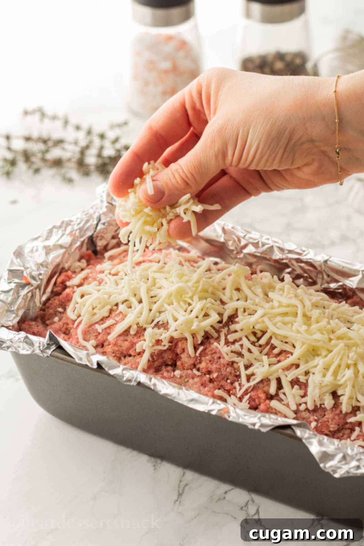 Hand sprinkling cheese on top of raw meatloaf.