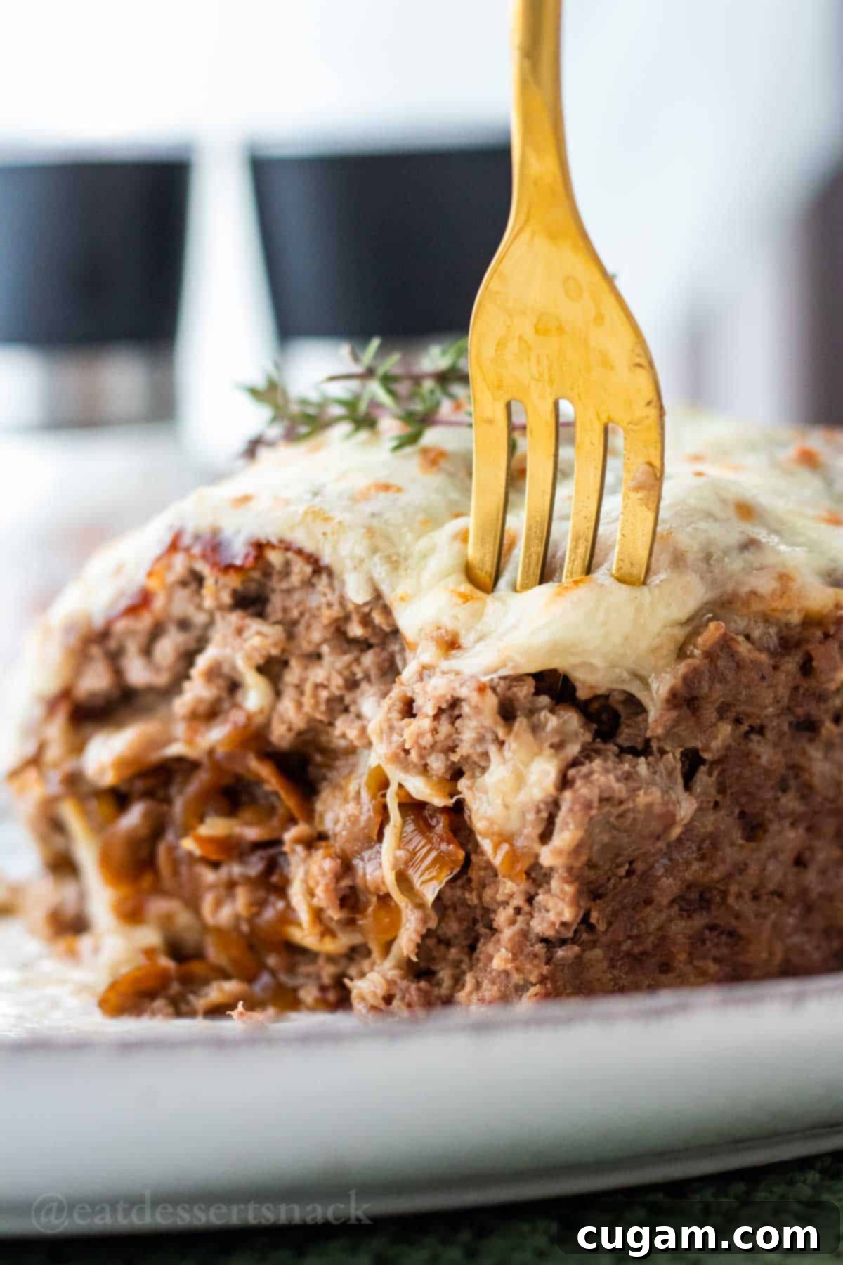 Fork poking into slice of cooked mushroom meatloaf with melted cheese and onions.