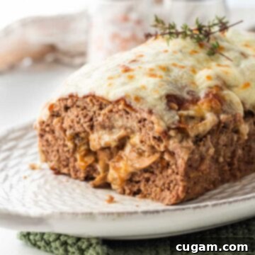 Cooked meatloaf stuffed with mushrooms and cheese on white platter with thyme on top.