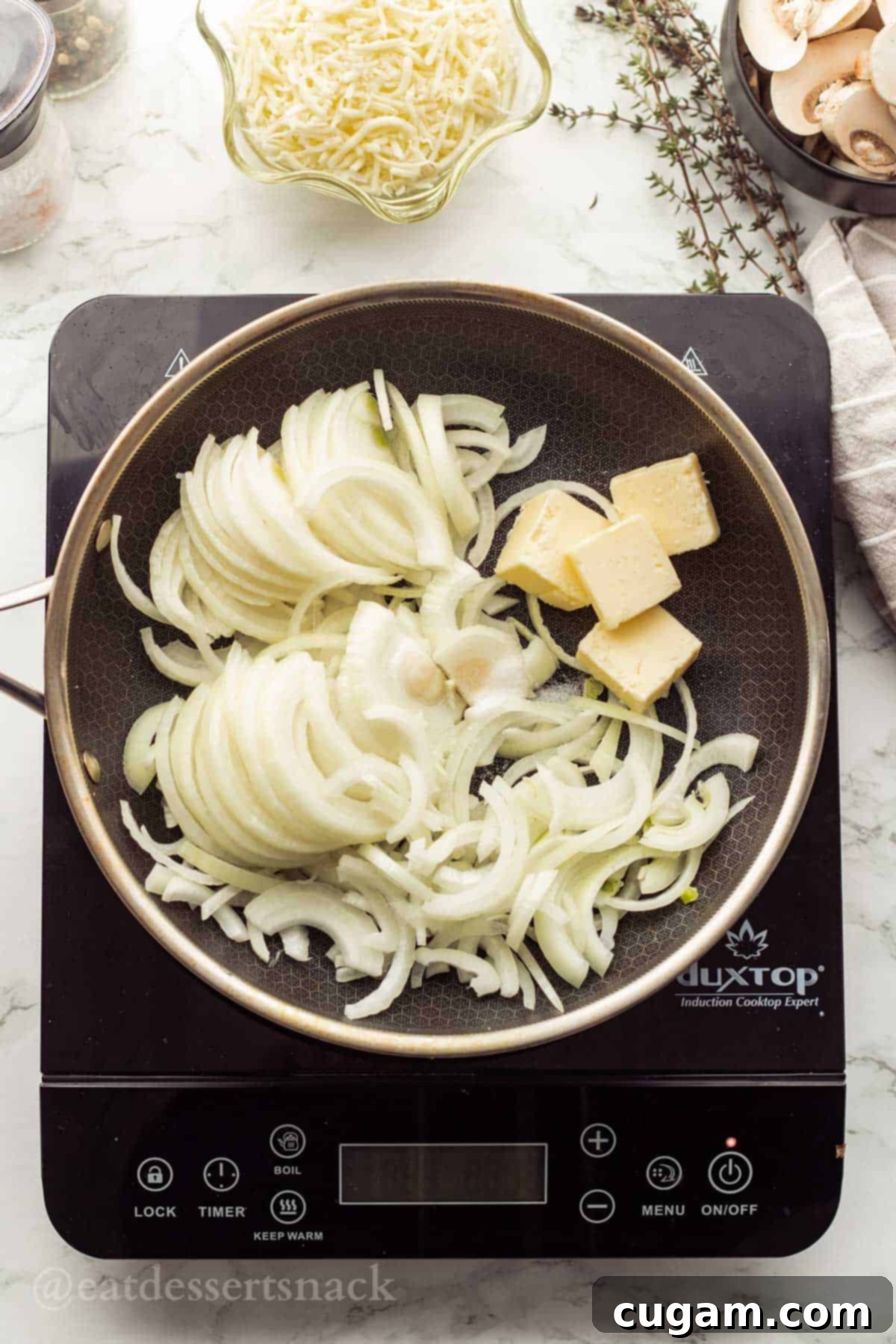 Raw onions with butter in metal pan on cooktop.