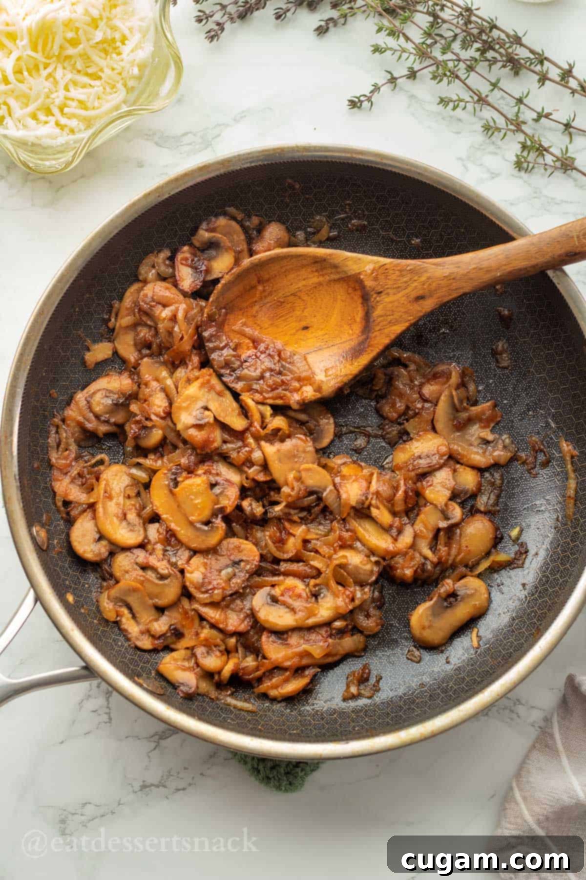 Cooked mushrooms and onions with wooden spoon in metal pan.