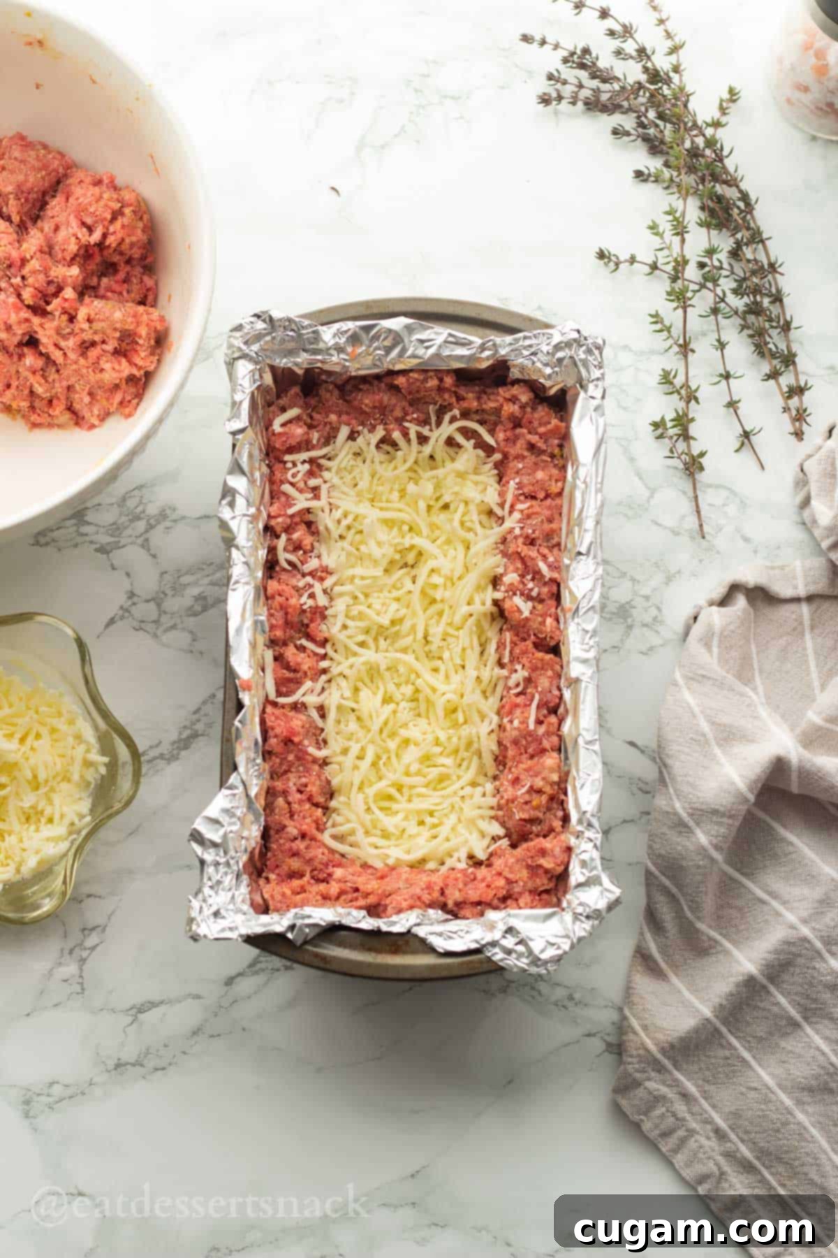 Cheese sprinkled in the bottom of a raw meatloaf boat in a pan.