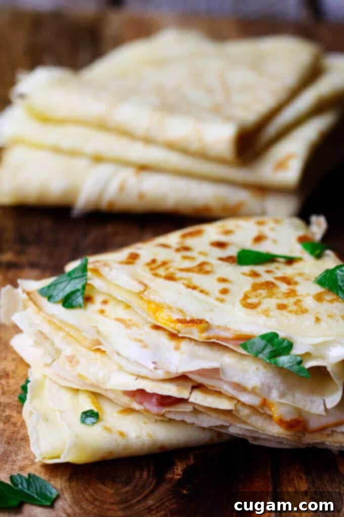 Three golden French crepes filled with melted cheese and ham, elegantly folded and stacked on a white plate