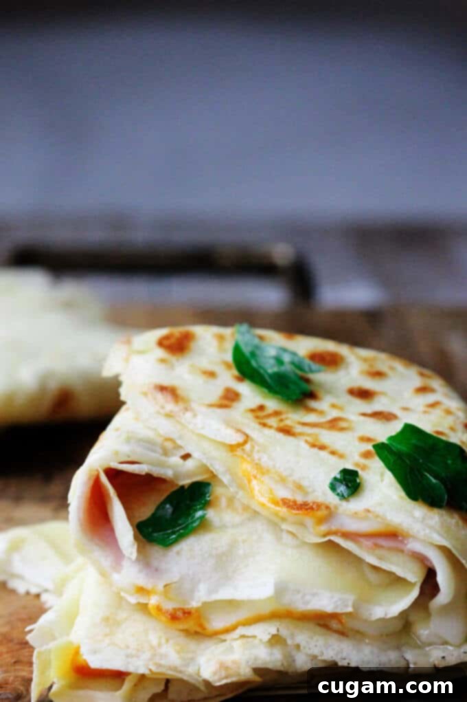 A close-up of a beautifully folded French crepe, revealing the warm, gooey ham and melted cheese inside