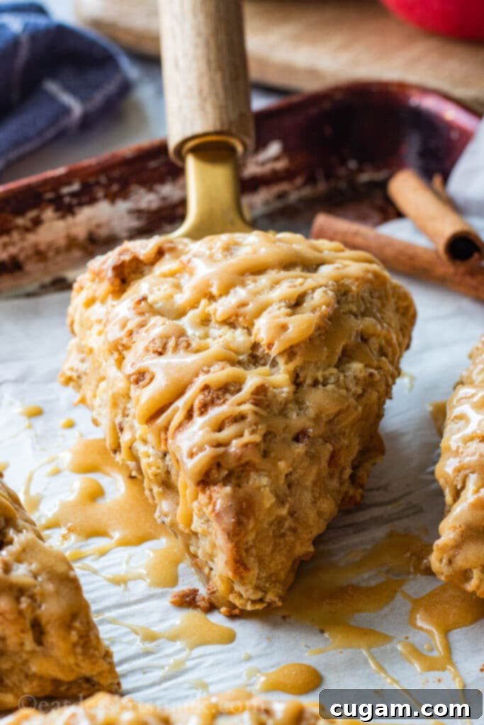 Baked Apple Cinnamon Scone on a spatula with a generous maple caramel glaze drizzle, ready to be served.