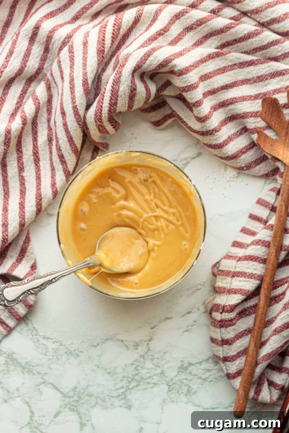 Smooth and creamy maple caramel glaze in a glass bowl with a metal spoon, perfectly blended and ready to drizzle over warm scones.
