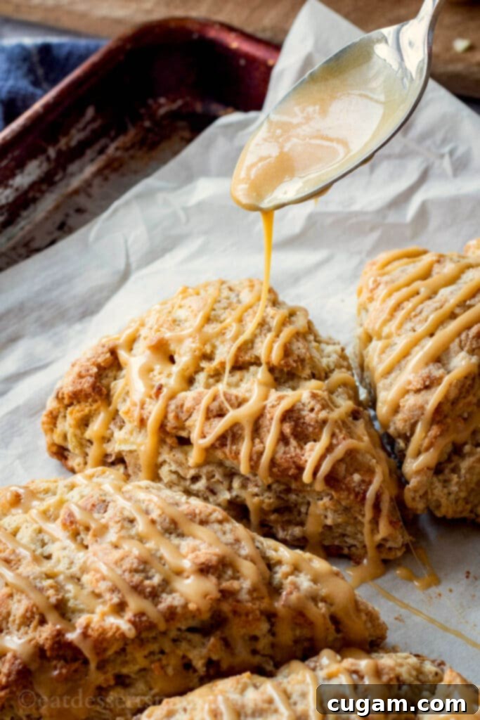 A delicious apple cinnamon scone being drizzled with a rich maple caramel glaze, capturing the moment of perfection.