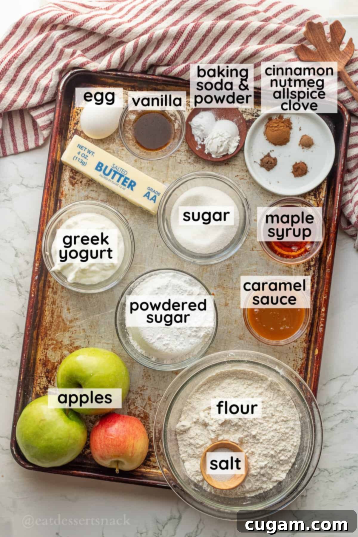 Labeled ingredients for maple caramel apple cinnamon scones in glass dishes on metal pan, including fresh apples, butter, Greek yogurt, and spices.
