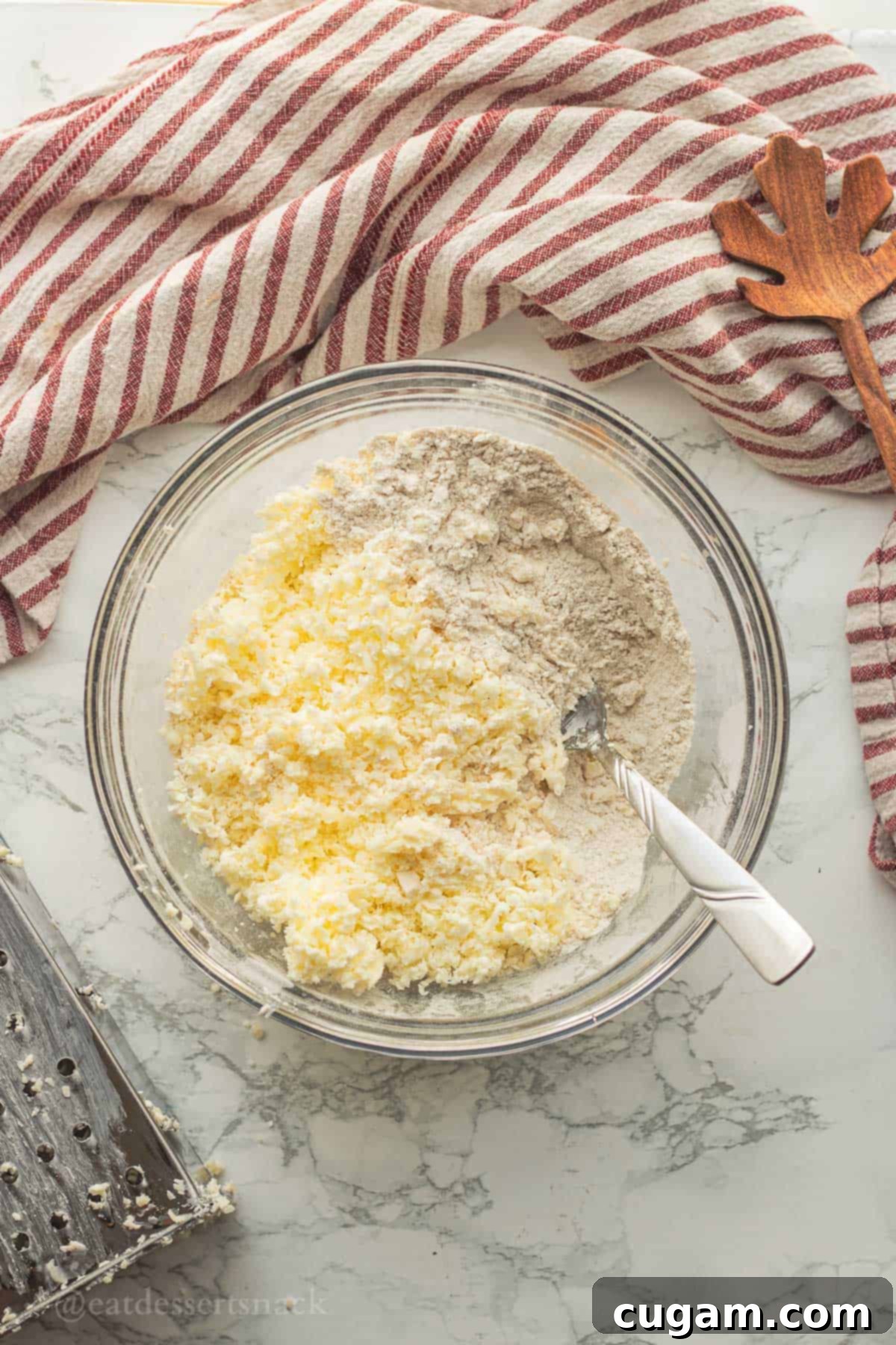 Finely grated frozen butter mixed into the dry ingredient mixture in a glass mixing bowl for apple cinnamon scones.