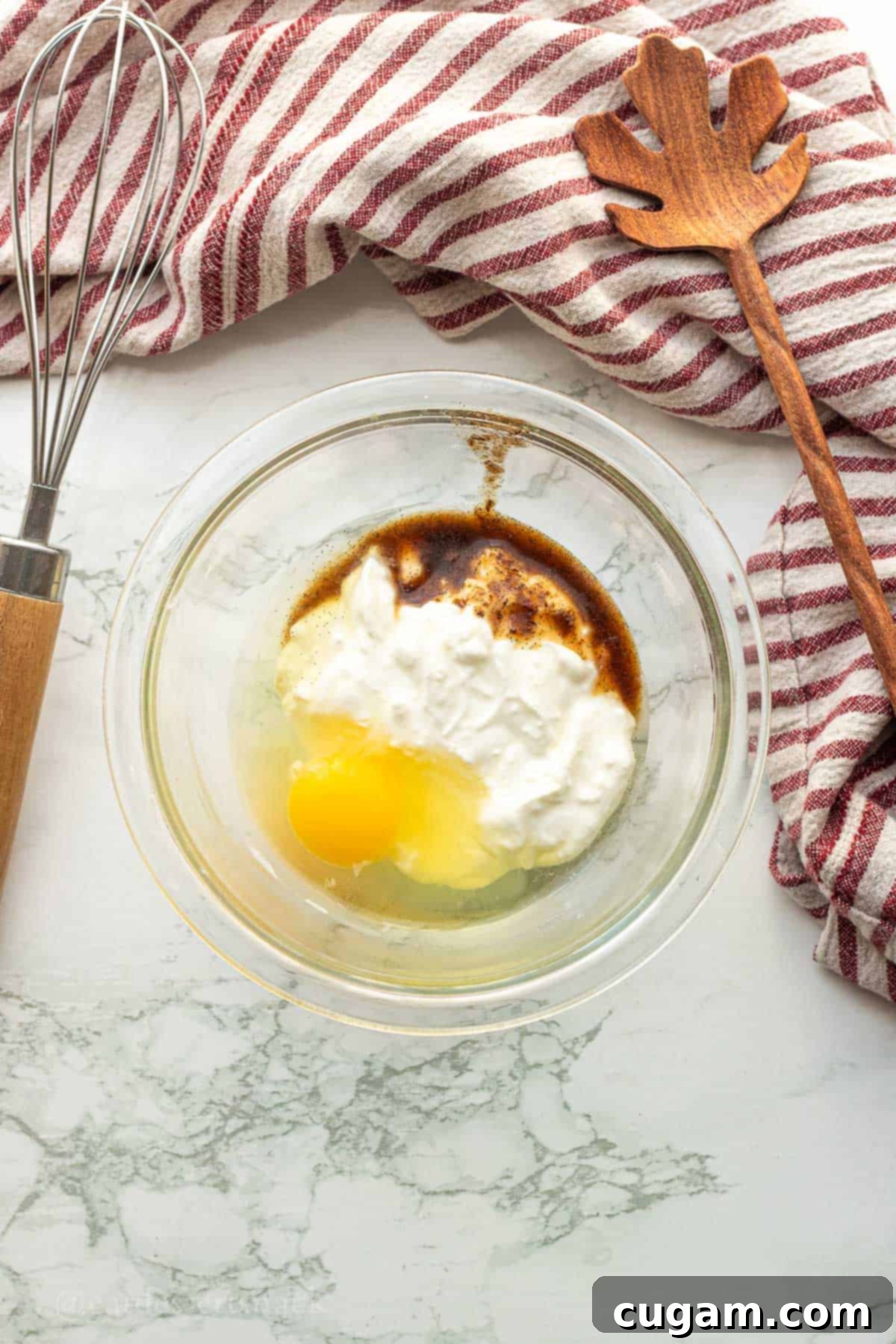 Wet ingredients for apple cinnamon scones: egg, vanilla extract, and Greek yogurt mixed together in a clear glass bowl.