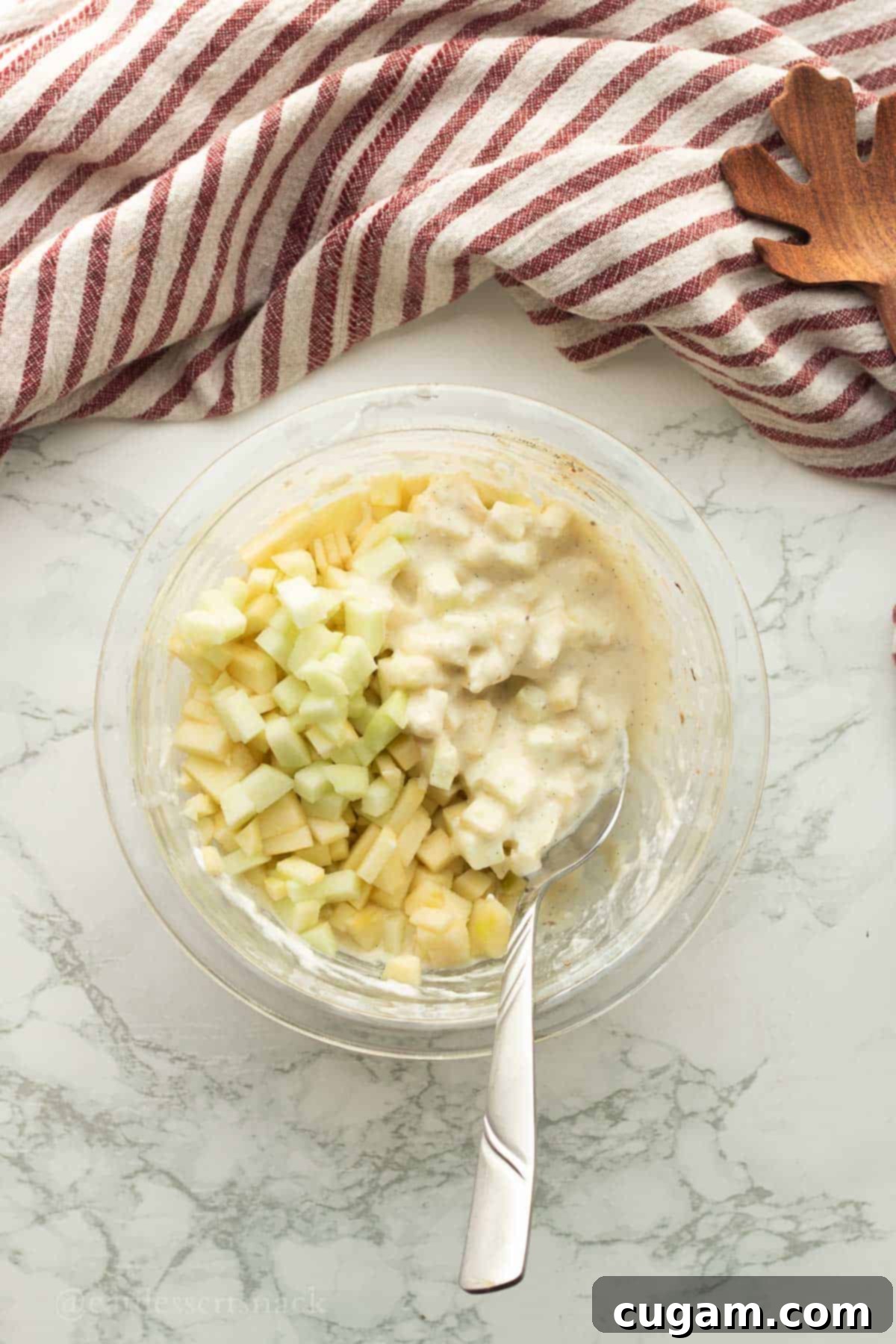 Finely chopped apples stirred into the wet ingredient mixture in a glass bowl with a metal spoon, creating a flavorful base for the scones.