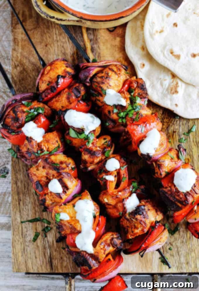 A vibrant platter of grilled Mediterranean Chicken Kebabs, artfully presented with fresh herbs and a generous serving of garlic yogurt sauce.