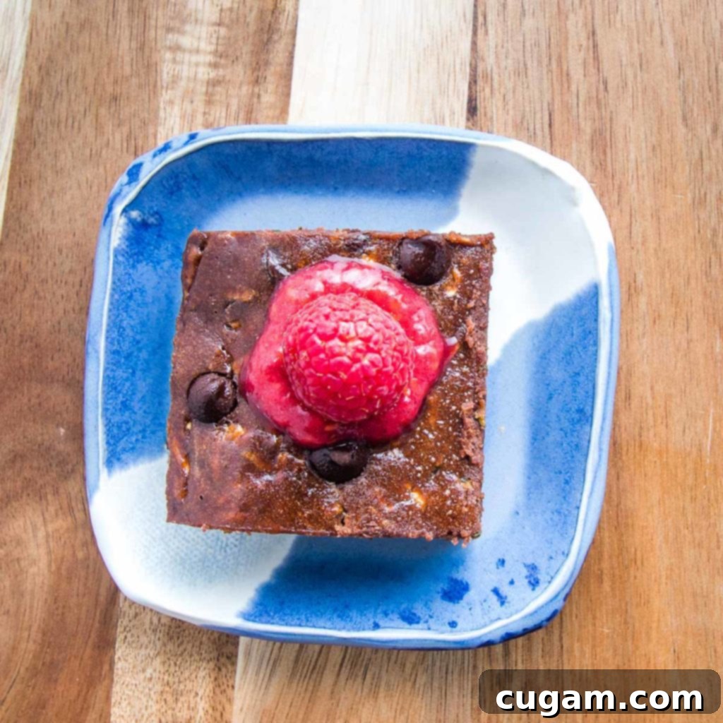 Super moist chocolate zucchini brownie on a bright blue plate with fresh raspberry sauce drizzled on top.