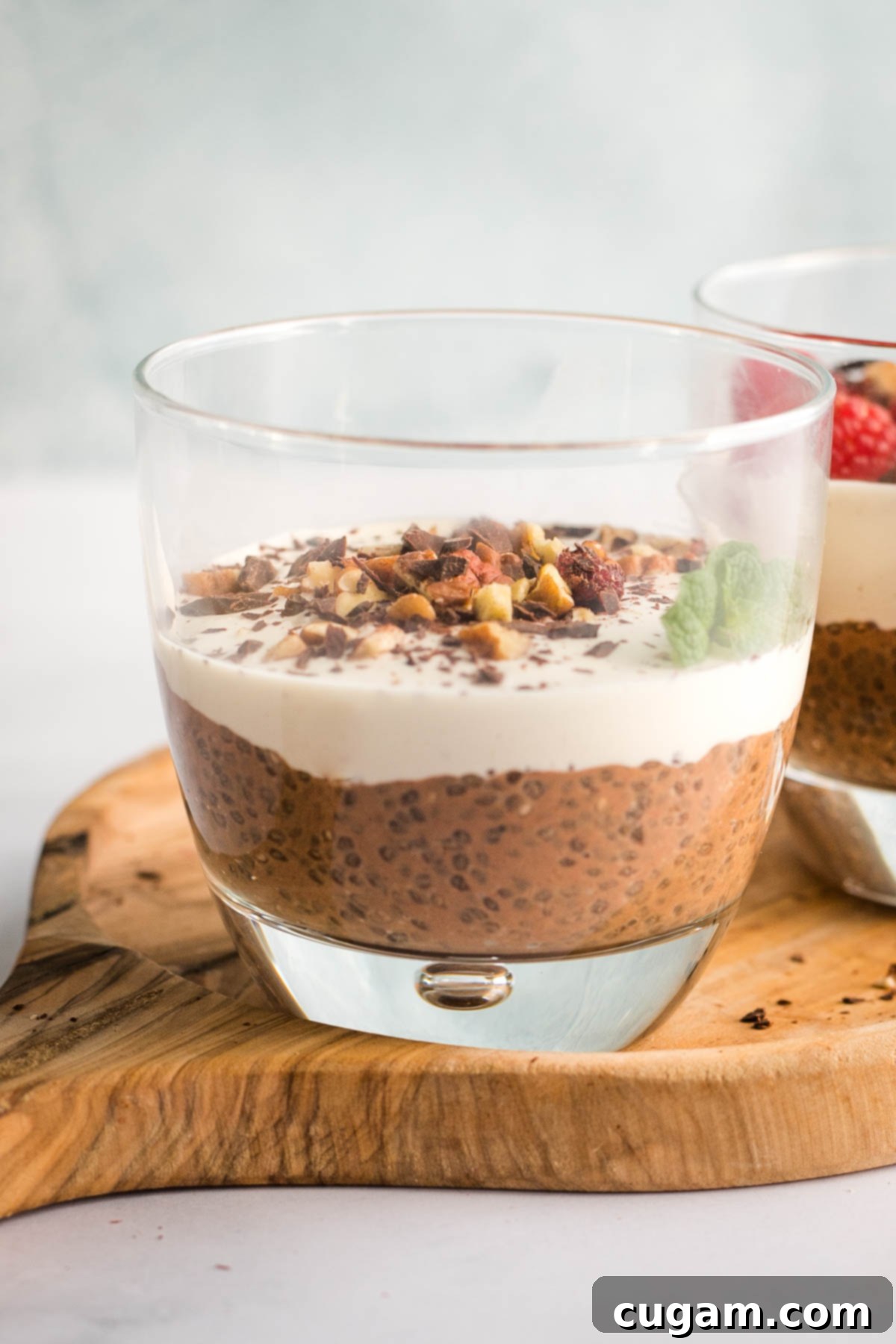 Chocolate chia pudding in the bottom of a glass, topped with cream and chopped nuts.