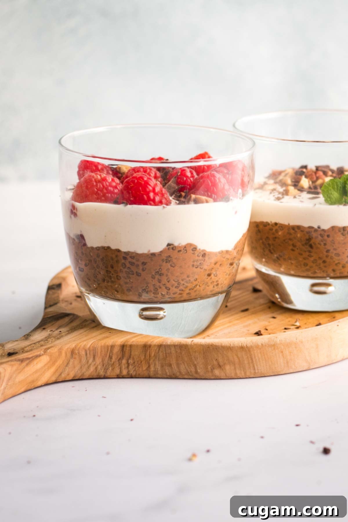Chocolate chia pudding in a glass, topped with cashew cream and fresh raspberries.