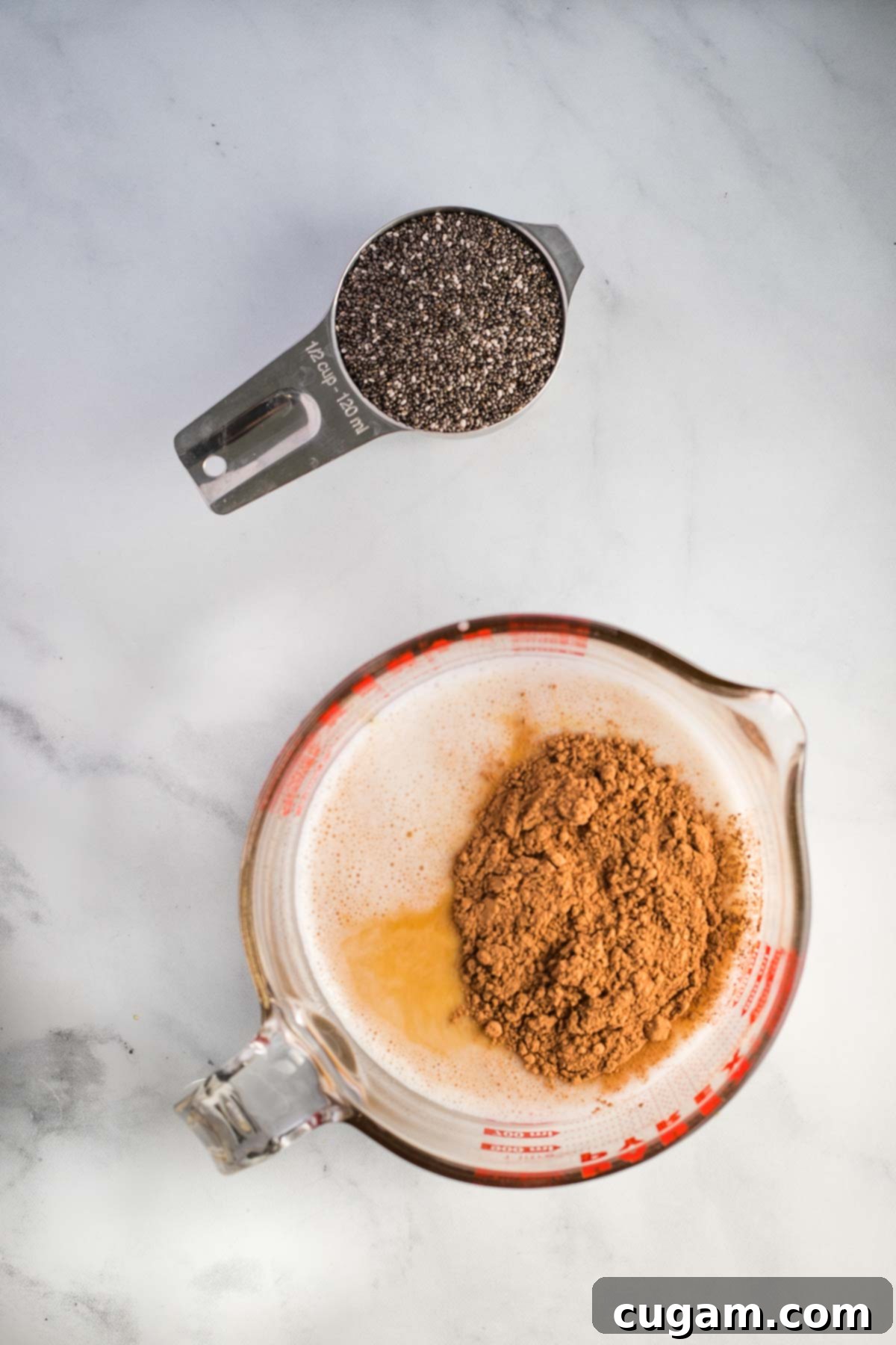 Dry measuring cup with chia seeds and liquid cup with plant-based milk, maple syrup and cacao powder.