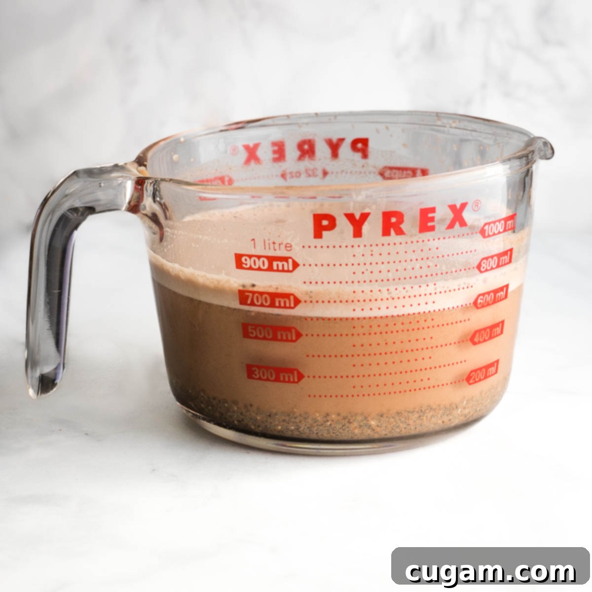 Glass measuring cup with chocolate milk at the top and chia seeds that sunk to the bottom.