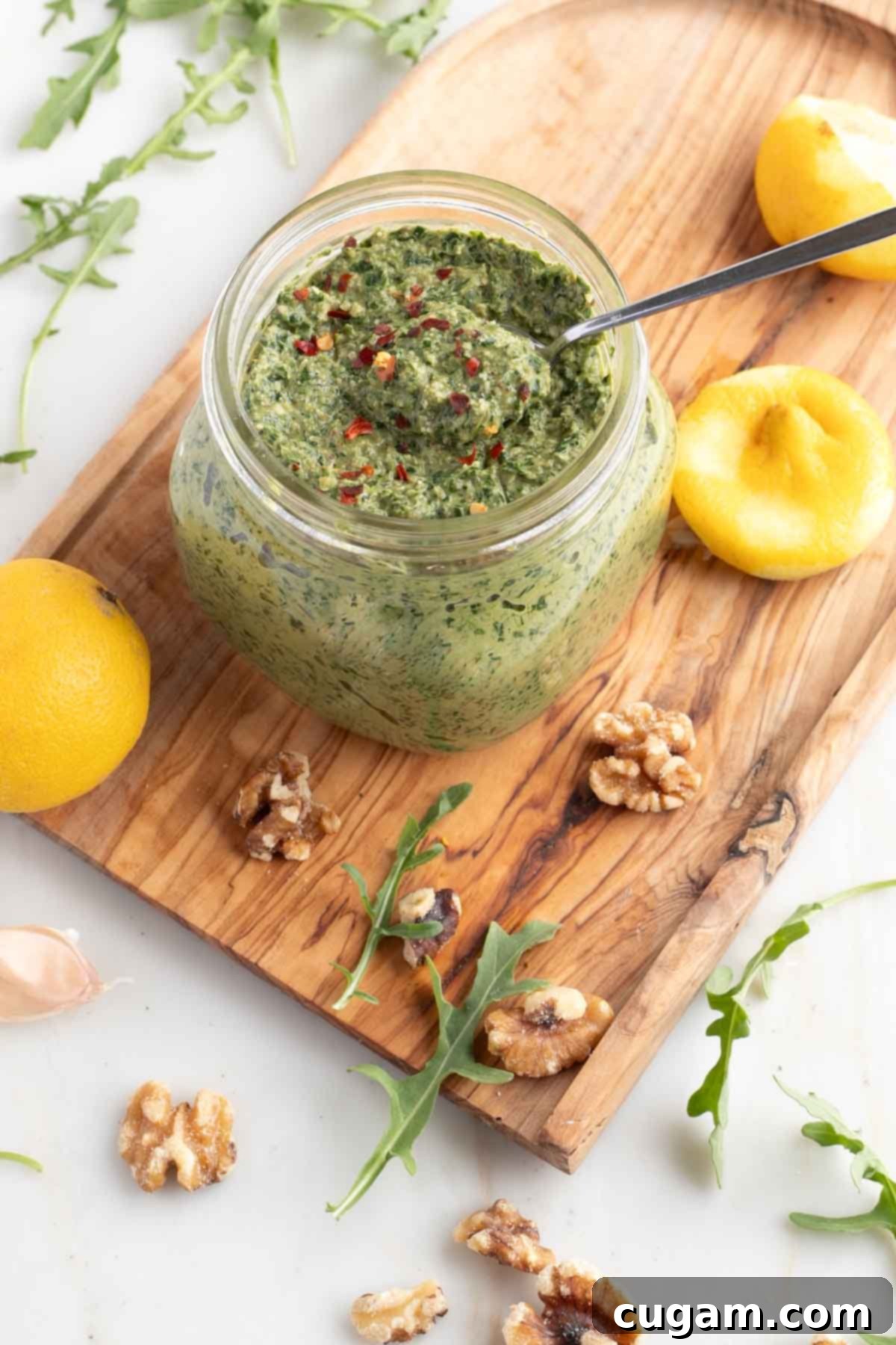 Vegan Arugula Walnut Pesto 2 Jar of pesto surrounded by arugula, walnuts, garlic and lemons.