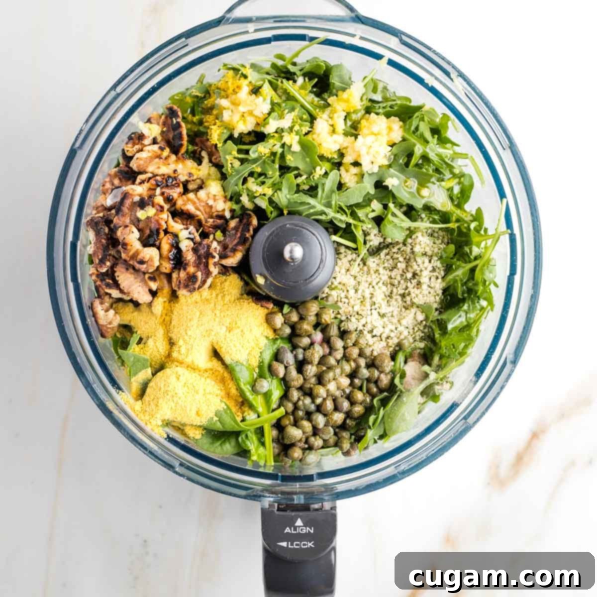 Vegan Arugula Walnut Pesto 5 Food processor bowl filled with greens, capers, hemp seeds, walnuts, lemon zest.