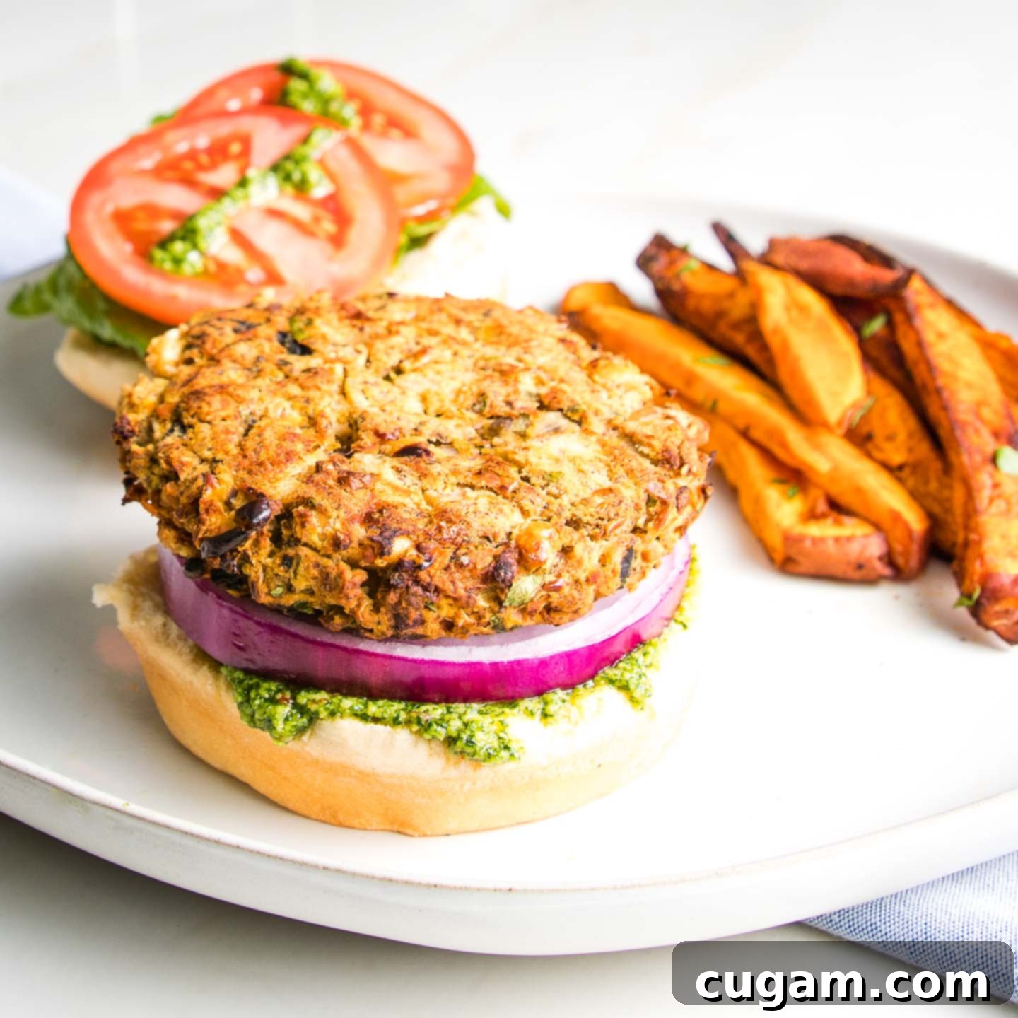 Open faced white bean veggie burger with purple onion and green arugula aioli plus lettuce and tomatoes with a side of crispy sweet potato fries. 