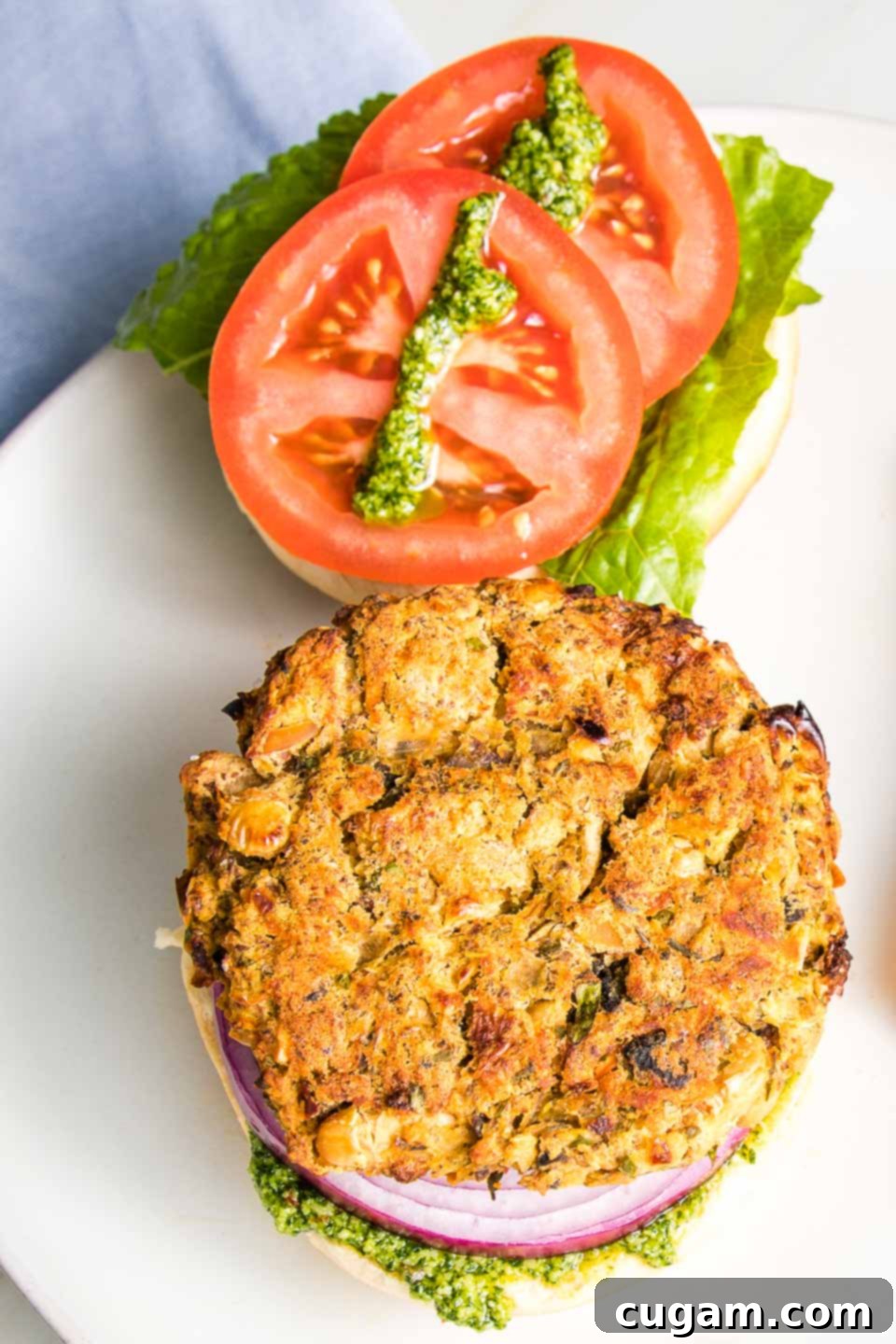 White bean burger on a bun with tomatoes, lettuce, onions and a drizzle of green sauce.