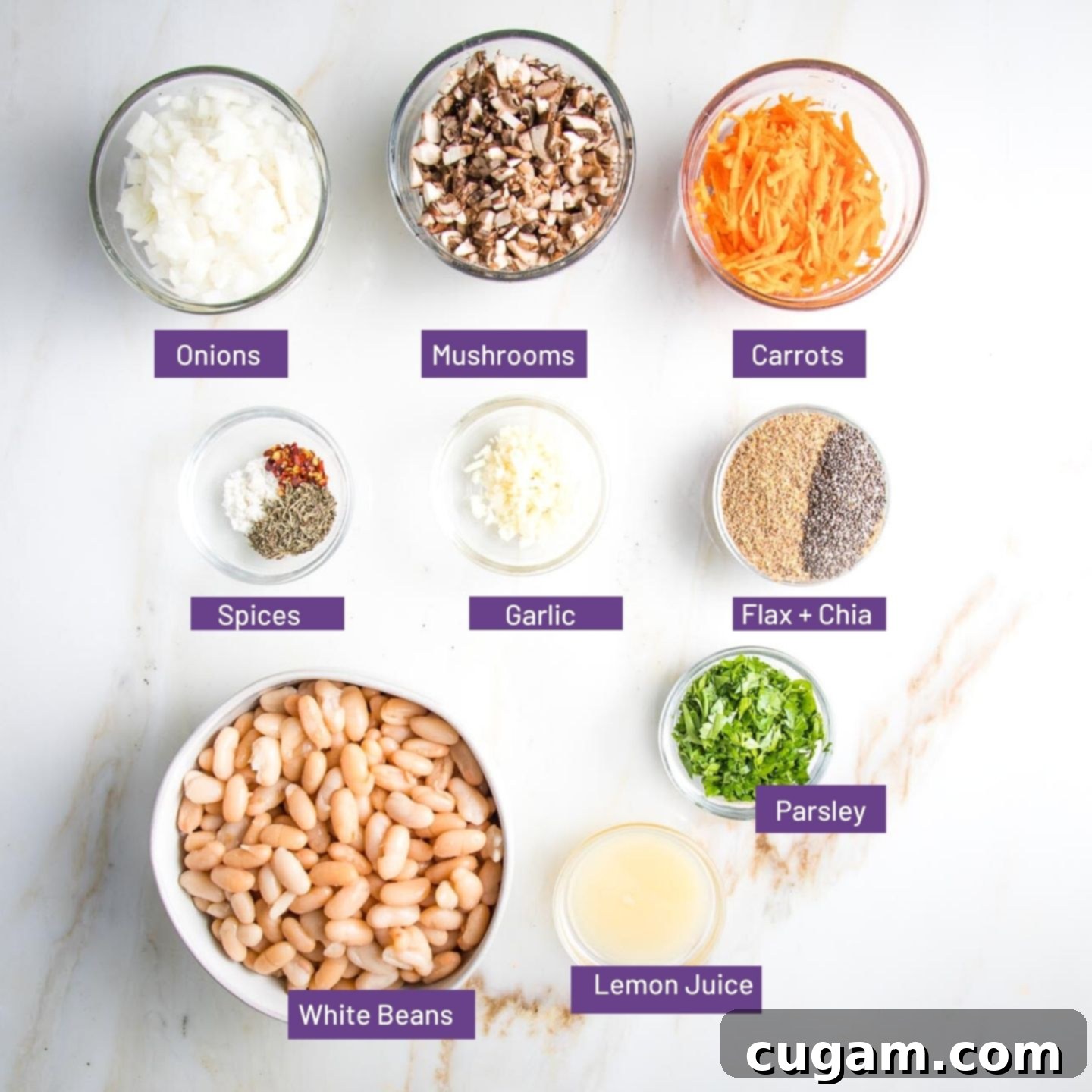 Ingredients for veggie burgers layed out in bowls: chopped onions, dices mushrooms, grated carrots, ground flax, chia seeds, garlic, spices, fresh parsley, lemon juice and a bowl of canellini beans.