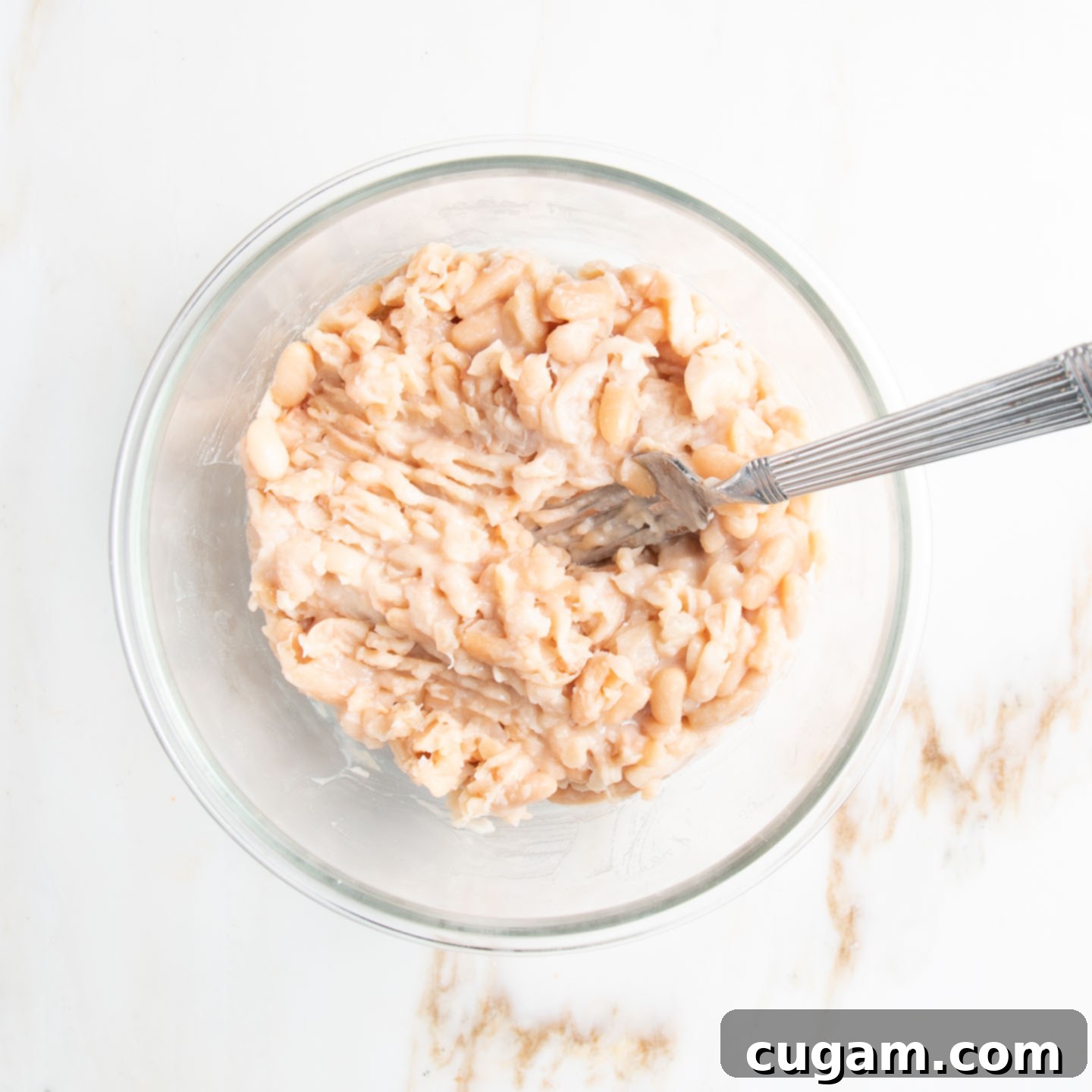 Mashed white beans in a bowl with a fork.