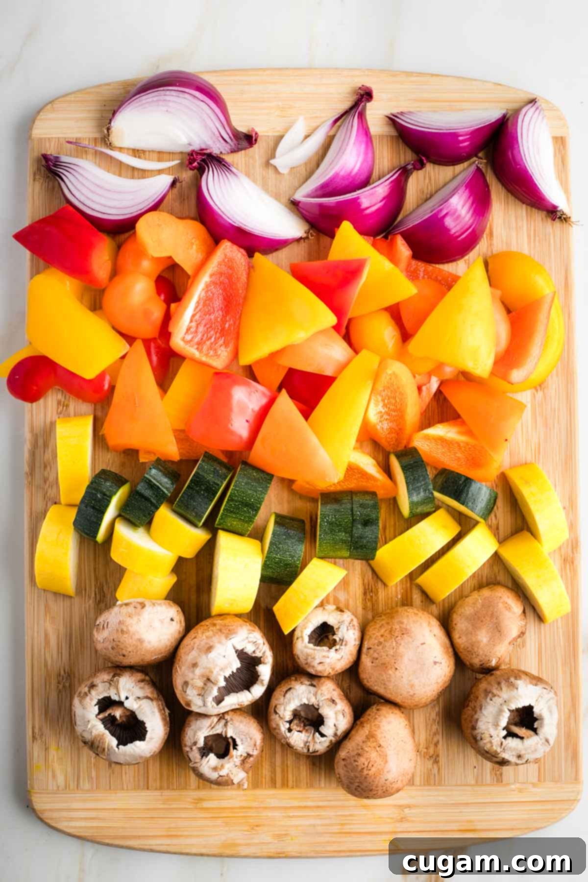 Mediterranean Harvest Skewers 4 Cutting board with big chunks of red onion, bell peppers, zucchini, yellow squash and baby bella mushrooms.