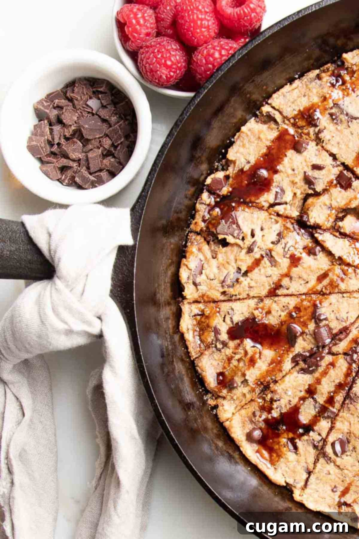 Delicious Vegan Gluten-Free Chocolate Chunk Skillet Cookie 2 Cast iron skillet filled with giant chocolate chunk cookie, garnished with fresh raspberries and a spoon.