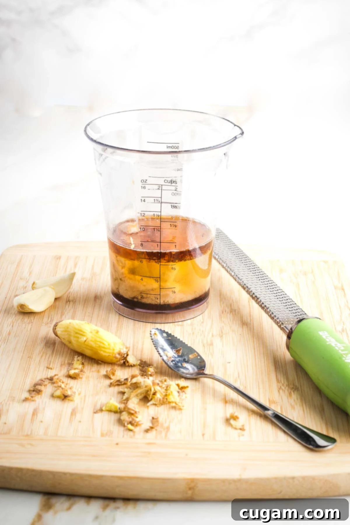 Knob of ginger peeled with a grapefruit spoon in front of a jar with liquid ingredients for dressing. 
