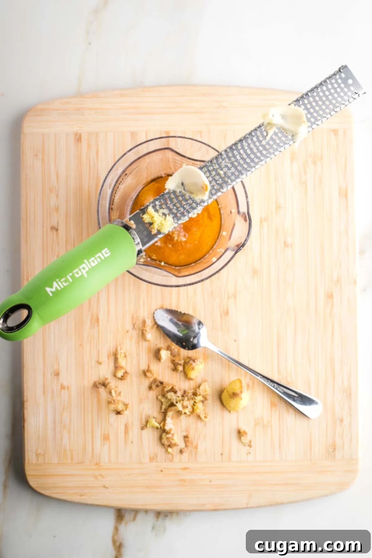 Grating garlic with microplane over a jar of dressing. Peels of ginger in the foreground.