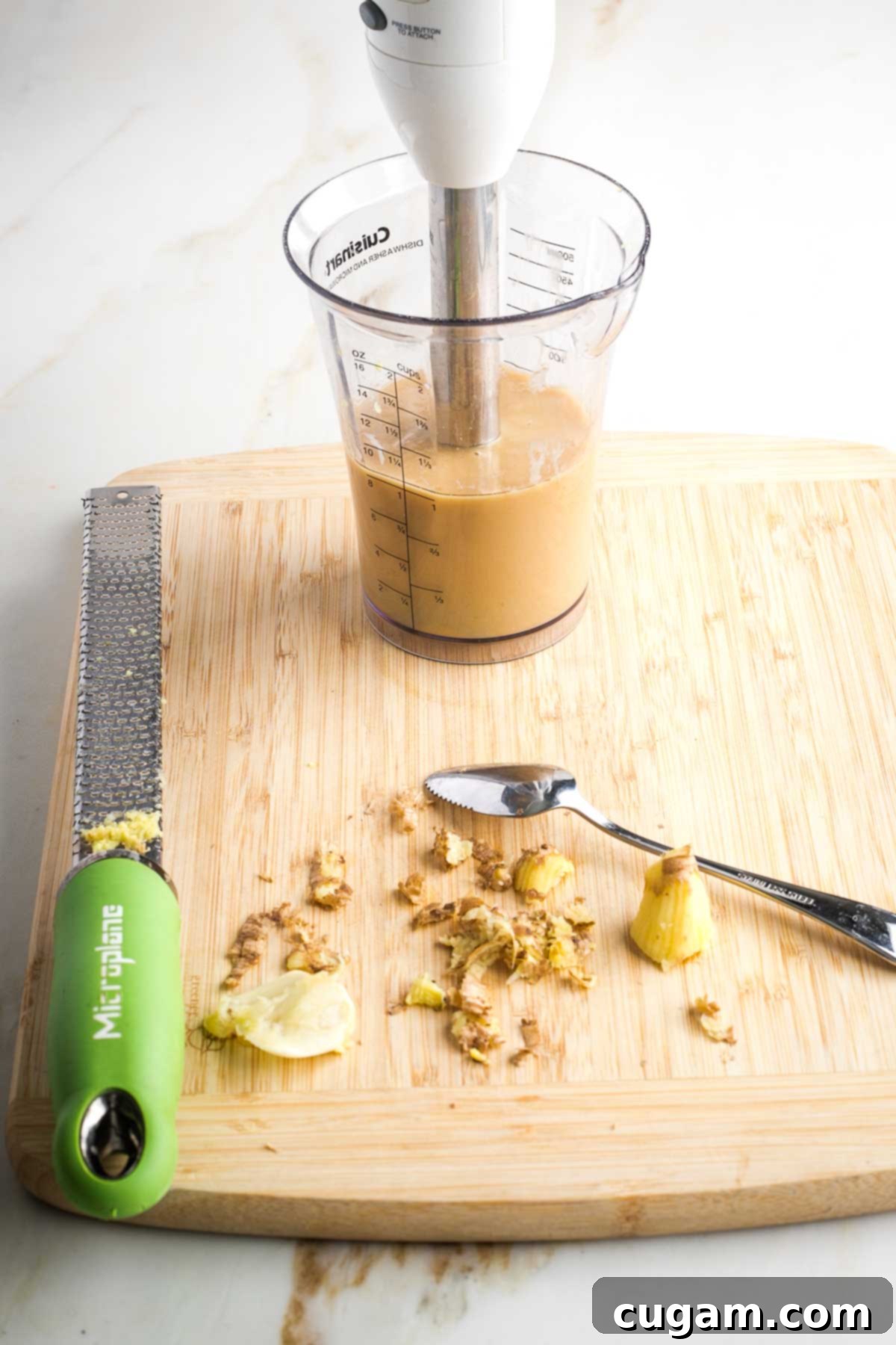 Immersion blender in a high container, blending light brown creamy dressing.