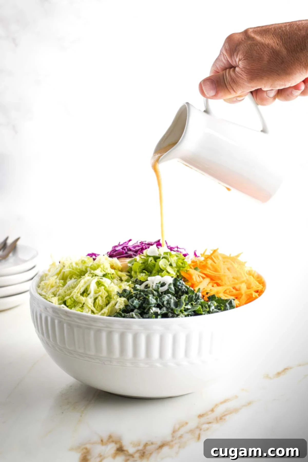 Creamy tan colored dressing poured over a bowl of colorful shredded veggies. 