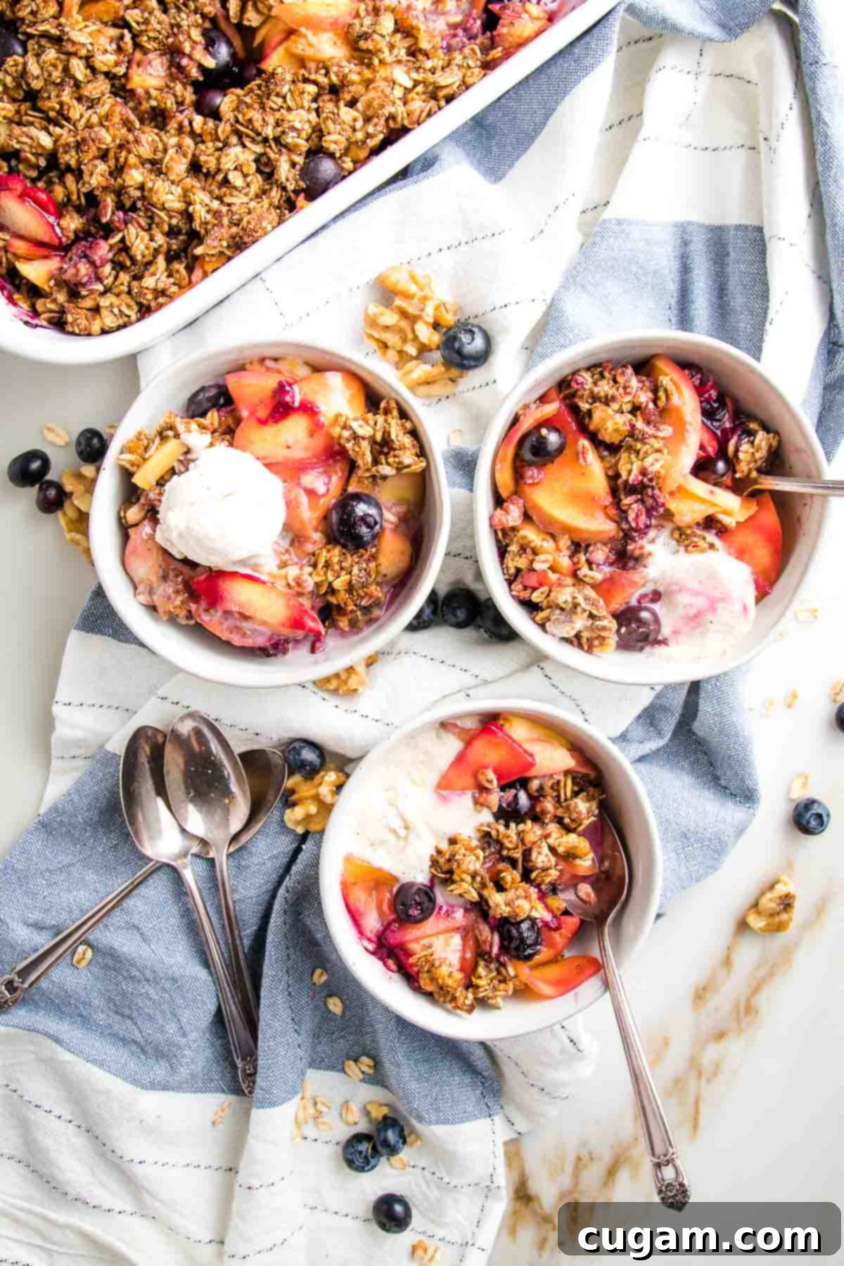 Three bowls filled with peach and blueberry crisp and topped with a dollop of ice cream.