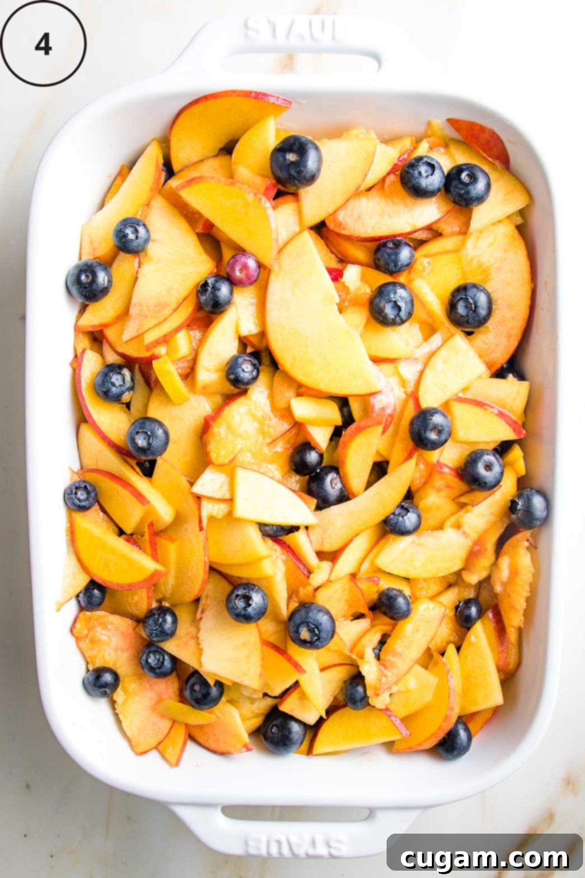 Sliced peaches and blueberries in a white baking dish.