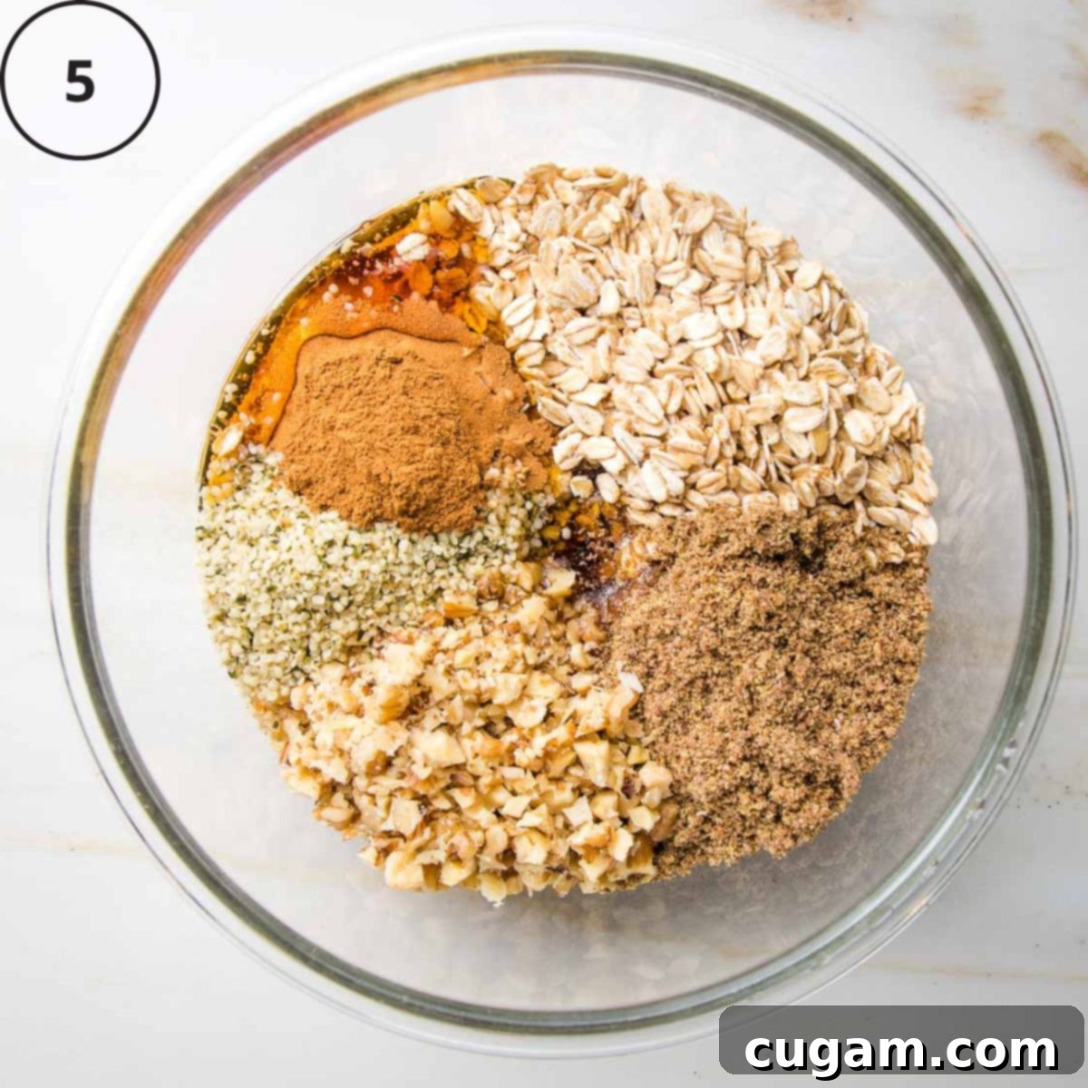 Glass bowl with sections of fruit crisp topping: oats, flax, nuts, seeds, cinnamon and maple syrup.