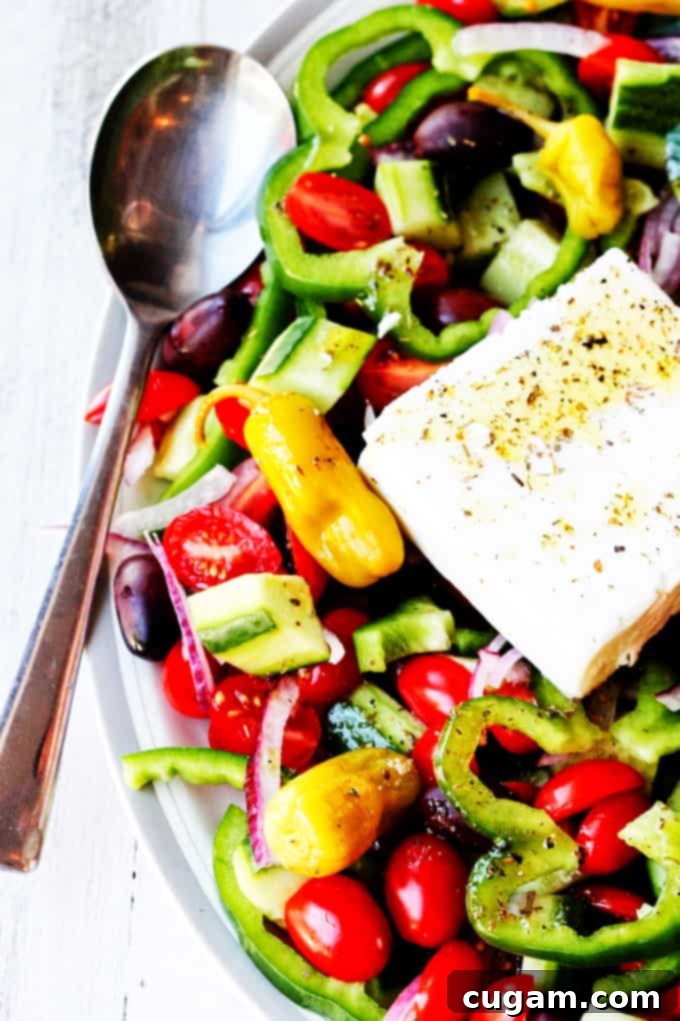 Close-up of Greek Horiatiki Salad with a large block of feta cheese and a spoon, ready to be served.
