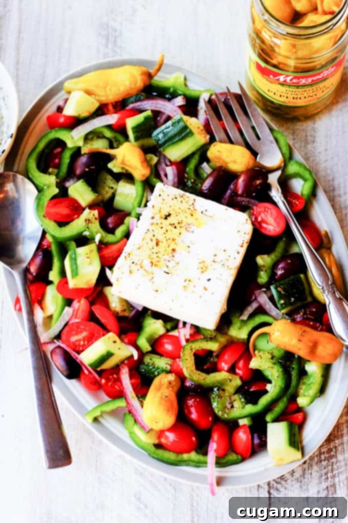 Horiatiki Salad on a plate with a jar of Greek peperoncini on the side, highlighting the optional spicy addition.