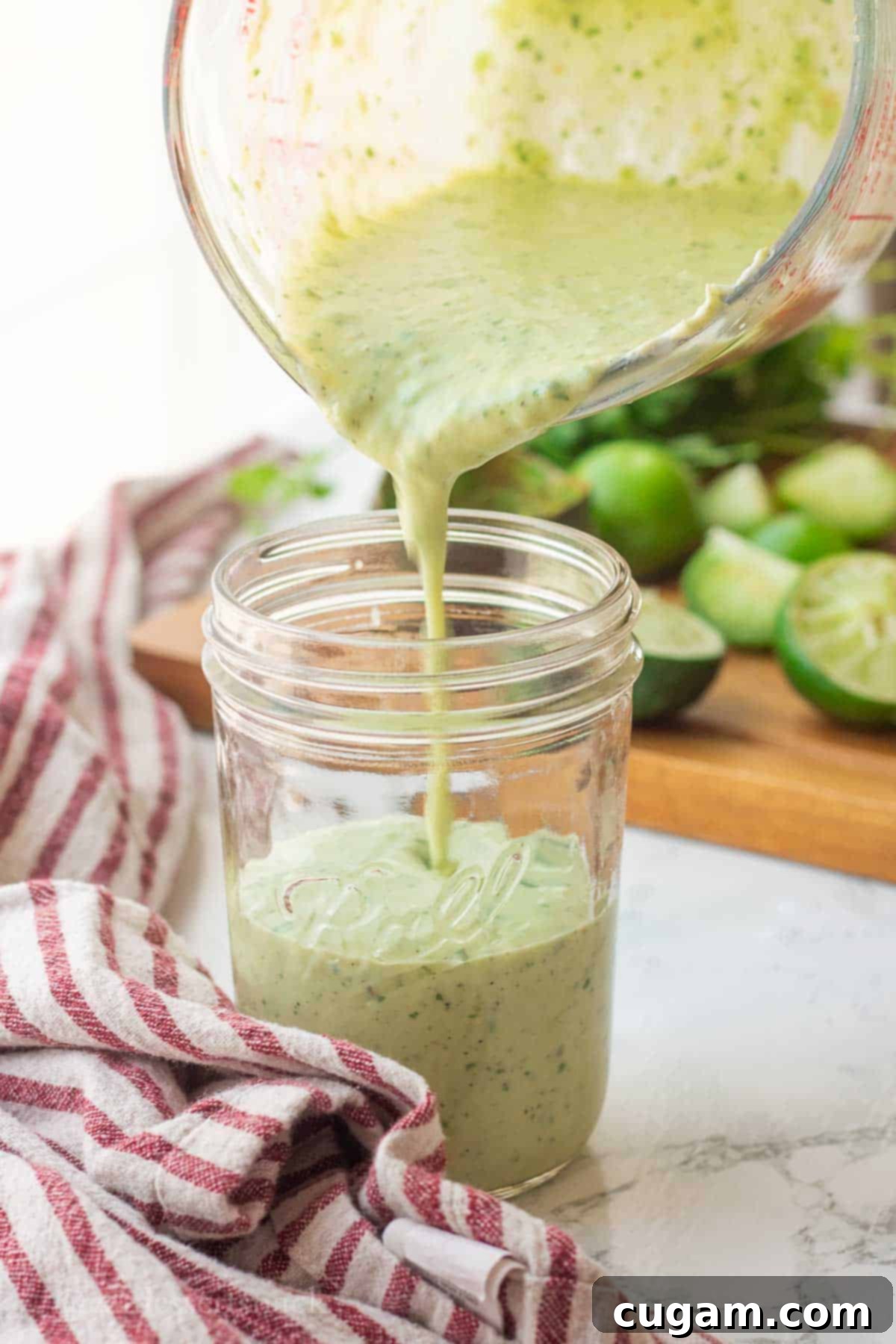 Smooth, vibrant green avocado lime ranch dressing being poured from a measuring cup into a clear mason jar, ready for refrigeration or serving.