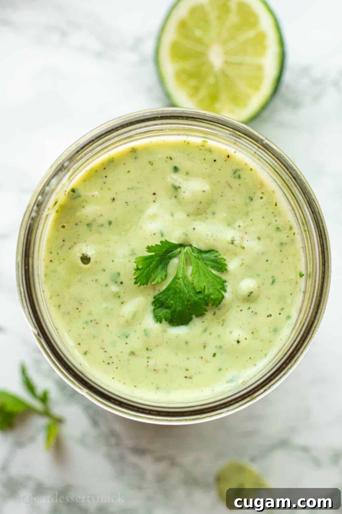 A full mason jar of homemade avocado lime ranch dressing, garnished with fresh cilantro, sits invitingly on a white marble countertop.