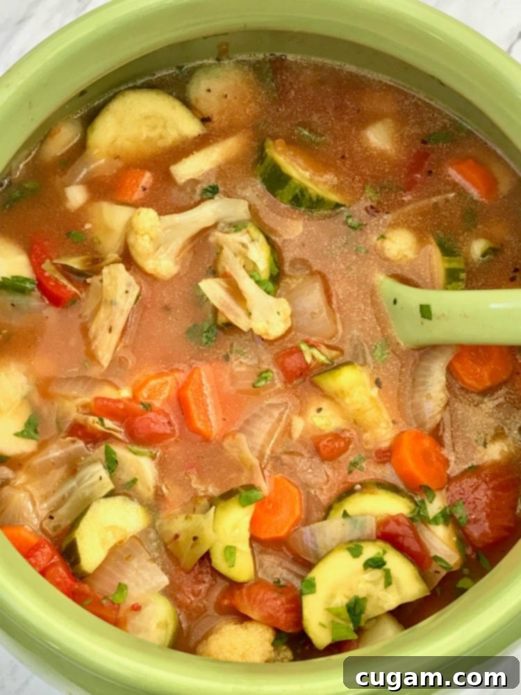 Lime green soup tureen filled with chunky roasted vegetable soup, garnished with fresh herbs.