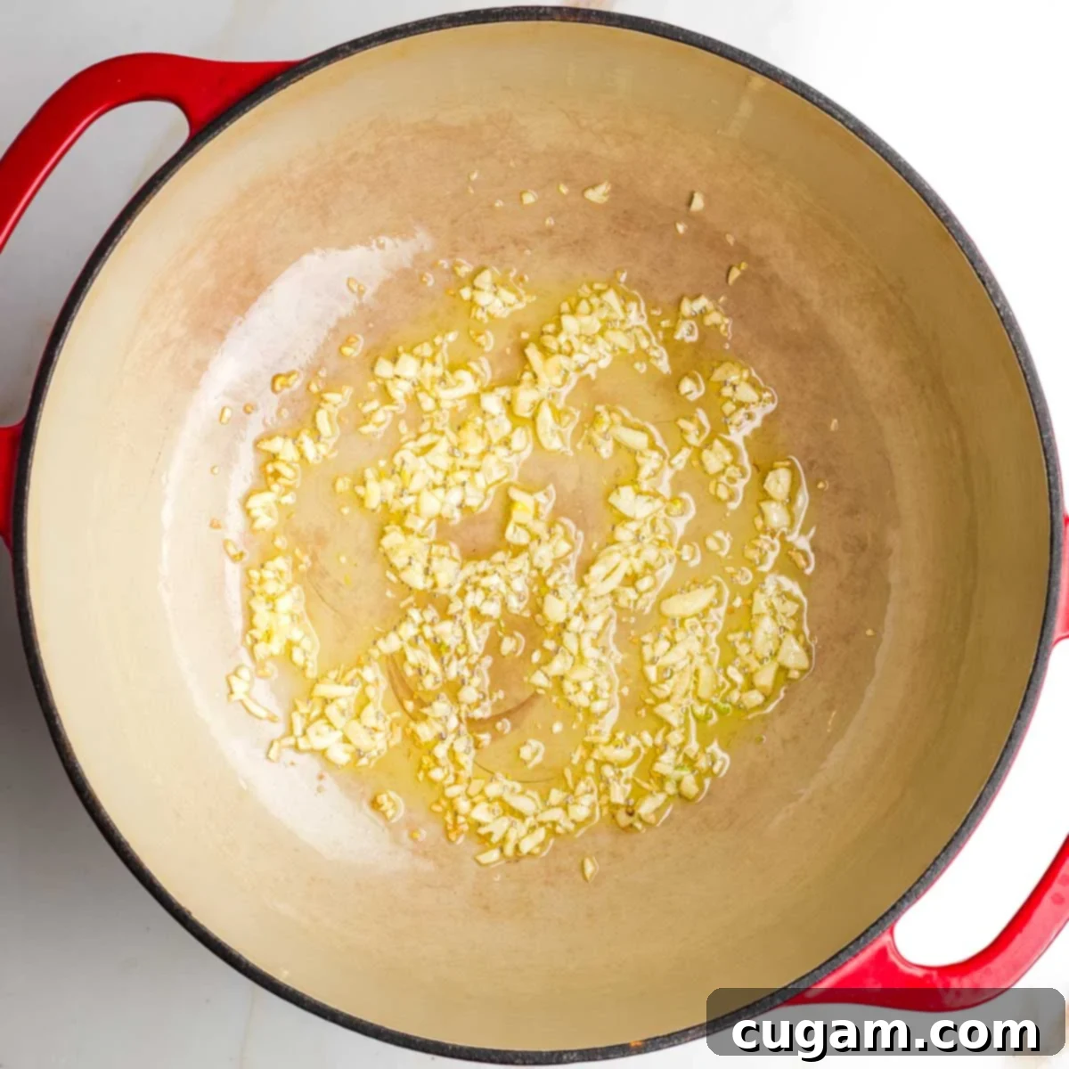 Garlic cloves sizzling in olive oil inside a Dutch oven.