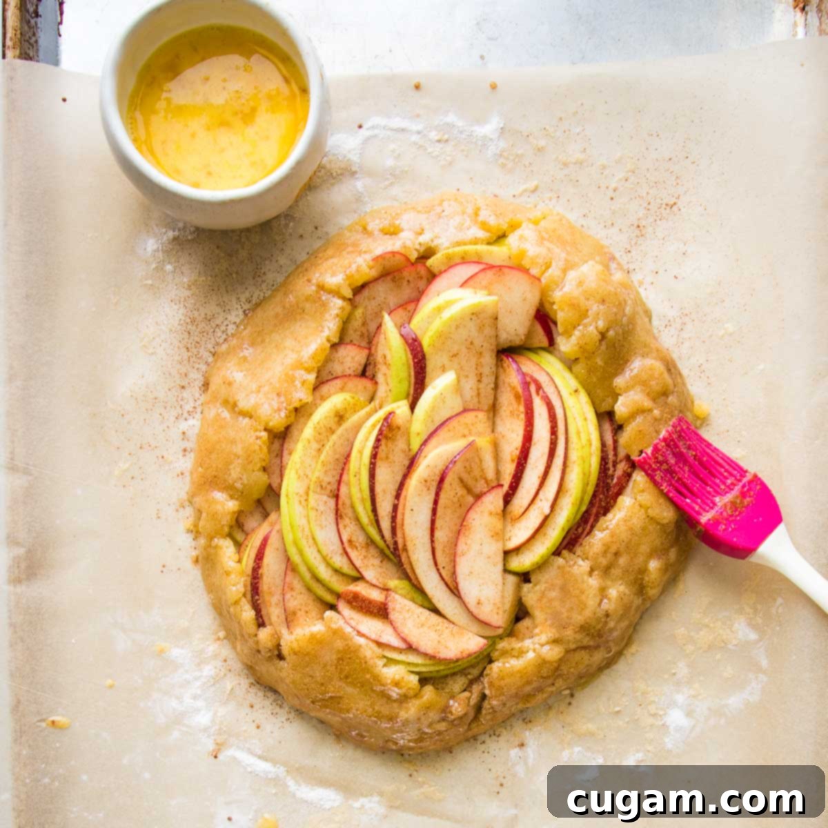 Pastry brush egg washing a rustic apple galette.