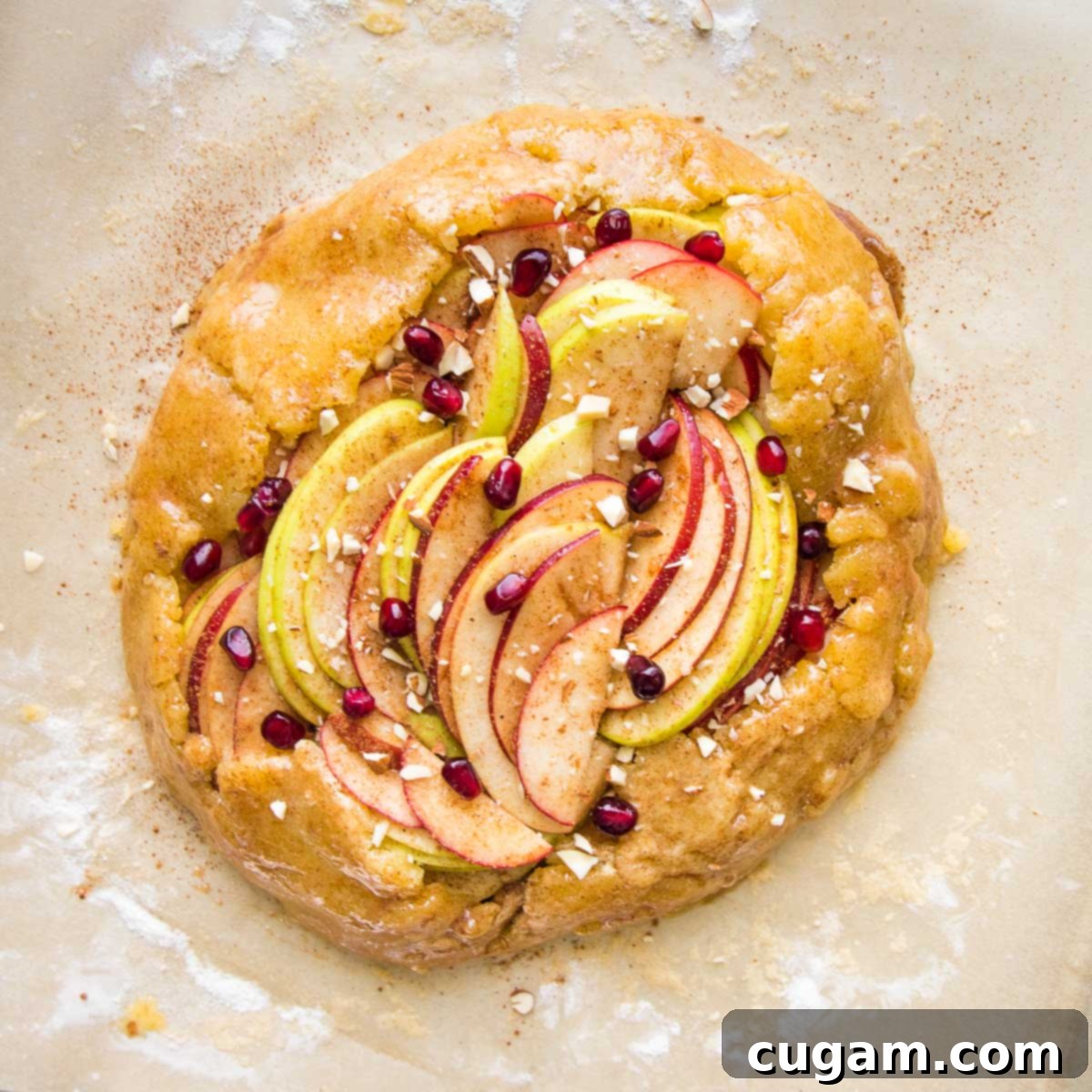 Free form galette with sliced apples, sprinkled with pomegranate seeds and nuts.